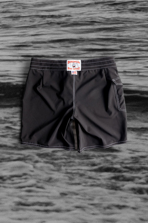 Back View of the 808 Boardshort in Black over a Black and White Image of Waves