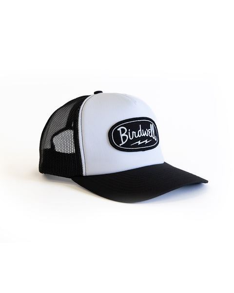 The Powerbird Foam Trucker - Black/White is a high-crown foam trucker hat with a mesh back, adjustable snapback, and a front patch reading 