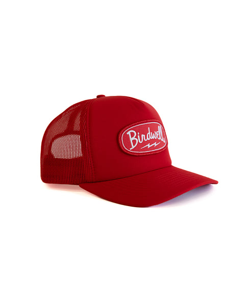 The Powerbird Foam Trucker - Red is a high-crown red trucker hat with a mesh back, curved brim, and a white embroidered Birdwell logo patch on the front, shown against a white background.
