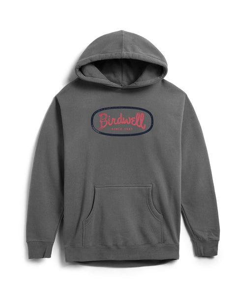The Mashed Potato Hoodie in Faded Black is a heavyweight hoodie with a relaxed fit and front pocket. The chest displays a navy blue oval screen-print with Birdwell in red script and Since 1961 in red below.