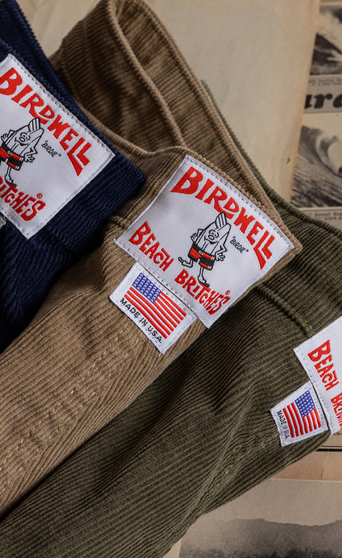Three stacked corduroy classic shorts. Close up showing the license plate patch. 