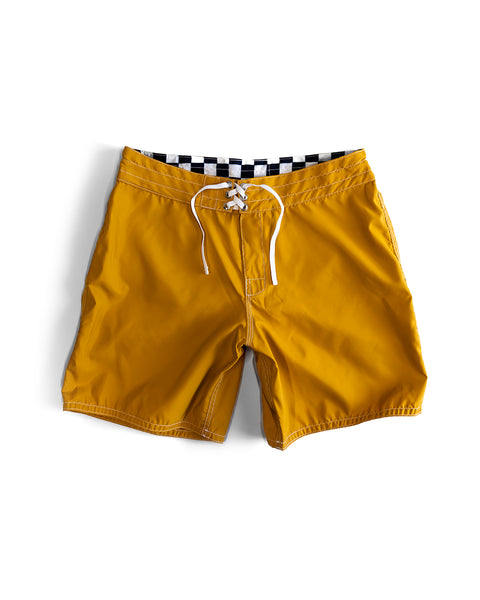 The 300 Boardshorts - Checkmate Gold feature bright yellow SurfNyl fabric, a black-and-white checkered waistband, and white drawstrings. Water-repellent and stylish, these boardshorts are ideal for beach days. Laid flat on a white background.