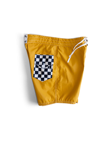 300 Boardshorts - Checkmate Gold feature yellow SurfNyl fabric, a black and white checkered pocket, white drawstring waistband, and a logo tag on the left. Water-repellent and shown against a white background.