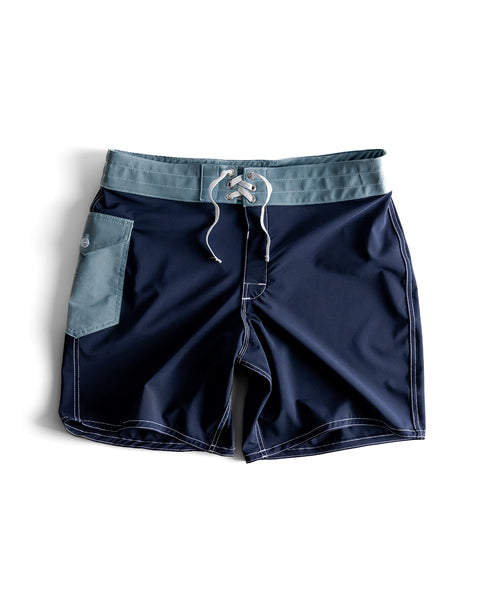 808 SurfStretch Pop Pocket Boardshorts in Navy/Federal Blue, featuring a light blue waistband and pocket, white drawstring and stitching, made in the USA with SurfStretch fabric, shown laid flat on a white background.