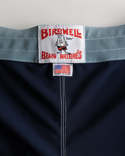 Close-up of the waistband of 808 SurfStretch Pop Pocket Boardshorts in Navy/Federal Blue, featuring a Birdwell Beach Britches label and a small American flag tag with 