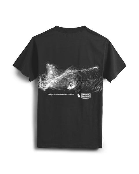 The Barrel T-Shirt - Faded Black is a heavyweight cotton tee, garment-dyed for softness. It features a white illustrated surfer on a large wave, a quote, and a small logo patch near the design’s bottom right.