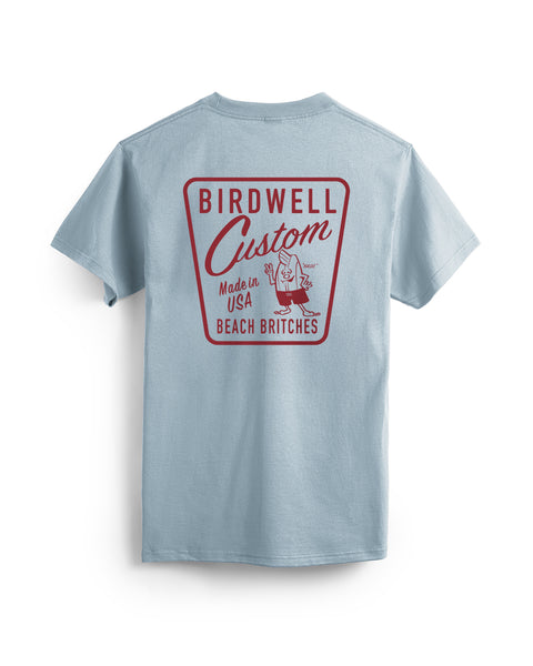 The Custom T-Shirt - Arctic Blue is shown from the back, featuring a large red cartoon bird with a board and 