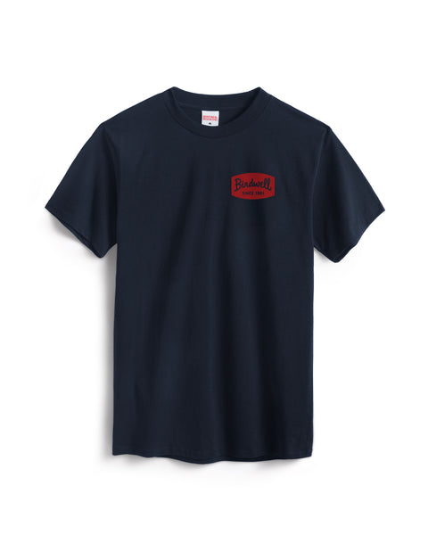 The Herald T-Shirt - Navy is a garment-dyed, plain navy short-sleeve cotton tee with a small red rectangular patch on the left chest that reads 