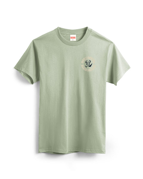 The Rounder T-Shirt - Desert Green is a light green, garment-dyed short-sleeve tee featuring a small circular logo with 