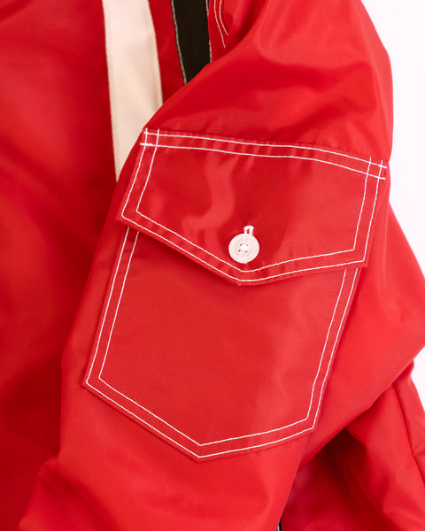 A close-up of the Quilt Lined Racing Jacket in red, showing its sleeve with a flap pocket, white stitching and a white button, set against a light background.