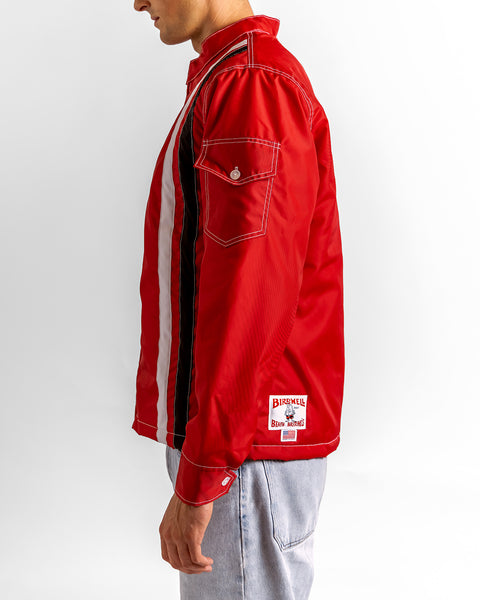 A person in the Quilt Lined Racing Jacket - Red/White/Black, featuring black and white vertical stripes, a buttoned sleeve pocket, white patch near the hem, and light blue jeans is shown from the side against a white background.