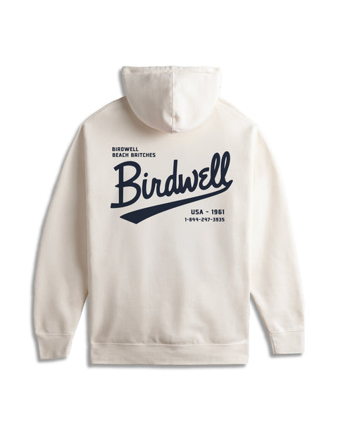 The Baller Hoodie - Bone is a cream-colored heavyweight hoodie with a relaxed fit, featuring “Birdwell” in bold navy script on the back and smaller text: “Birdwell Beach Britches,” “USA - 1961,” and a phone number.