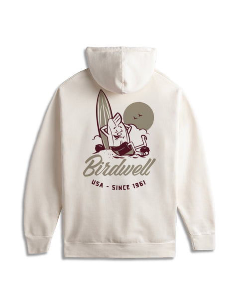 The Pau Hoodie - Bone is an off-white relaxed fit hoodie with a back screen-print of a smiling surfboard on the beach, sun and birds, plus “Birdwell USA - Since 1961” text.