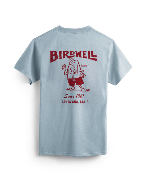 The 61 T-Shirt - Arctic Blue is a heavyweight, garment-dyed 100% cotton tee with a red “BIRDWELL Since 1961 SANTA ANA, CALIF.” graphic and a cartoon surfboard-head character waving on the back.