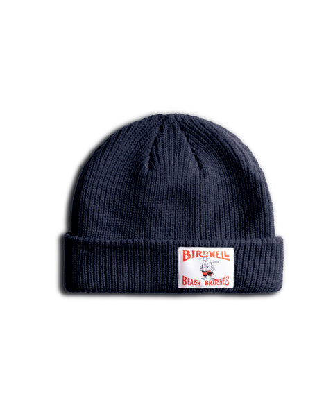 The License Plate Watchcap - Navy is a dark blue ribbed beanie with a folded brim and a white rectangular patch featuring red 