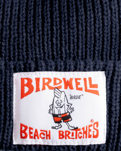 A close-up of the License Plate Watchcap - Navy shows its classic ribbed knit and a white patch label with 