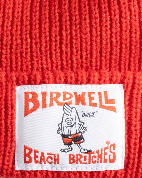Close-up of the License Plate Watchcap - Red knit fabric, featuring a white Birdwell patch with orange lettering and a cartoon bird character in red shorts.