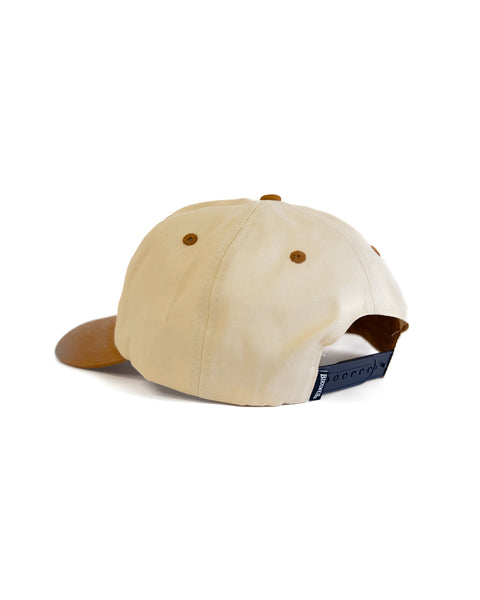The Tourist Twill Snapback - Bone/Brown is a 5-panel beige cotton hat with a brown brim, brown button and eyelet details, plus a black adjustable strap at the back featuring a small sewn patch logo tag.