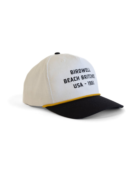 The Trademark Hemp Snapback - White/Black is a 5-panel baseball cap featuring white and black colors with a yellow brim accent. The front has direct black embroidery that reads 
