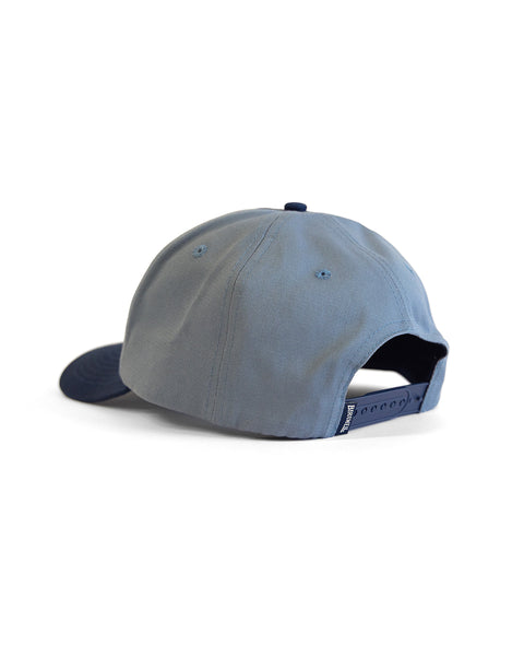 The Script Twill Snapback in Federal Blue/Bone is a 5 panel cotton hat shown from the back, highlighting its adjustable snapback strap and a small fabric tag near the closure, set against a white background.