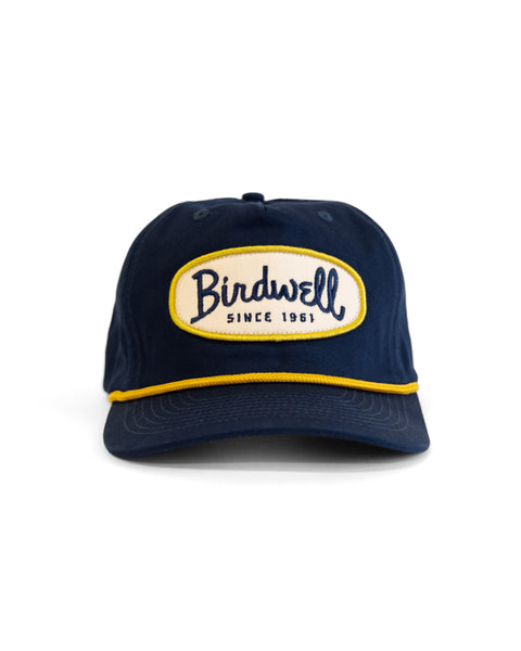 The Potato Patch Twill Snapback - Navy is a high-crown cotton hat with a yellow-trimmed brim, and a front patch stating 