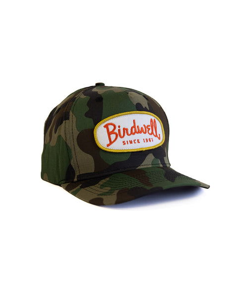 The Potato Patch Twill Snapback - Woodland Camo is a 5-panel cotton hat with a camo pattern, curved brim, and a front white patch that reads 
