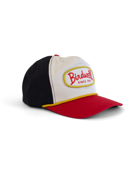 The Potato Patch Twill Snapback in bone, red, and black features a cotton build, high crown, red brim, and a front patch trimmed in yellow that reads 
