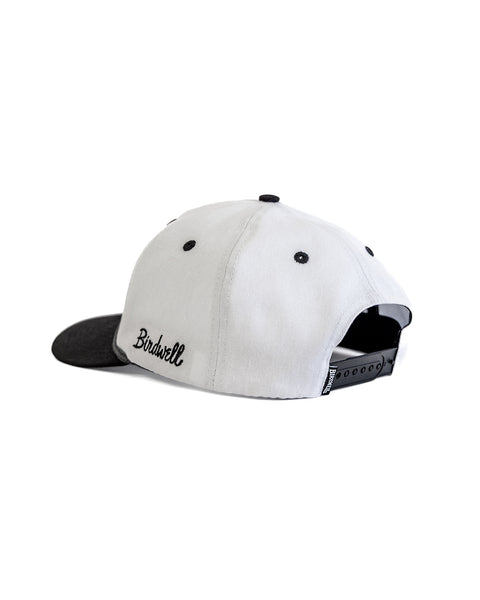 The Big B Twill Snapback - White/Black is a white 5-panel cotton hat with a black brim, button, and eyelets. It has an adjustable snapback strap and features 
