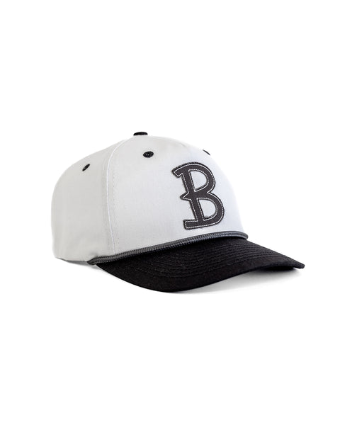 The Big B Twill Snapback - White/Black is a cotton 5-panel hat featuring a black brim, large black embroidered B on the front, and black accents on the seams and eyelets for a classic sporty look.