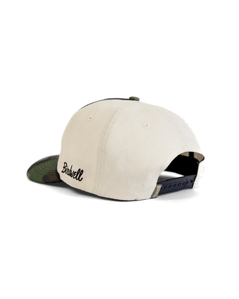 A woodland camo 5 panel snapback baseball cap viewed from the back, featuring a black adjustable strap and the word Birdwell embroidered in black on the side. Product name: Big B Twill Snapback - Woodland Camo.