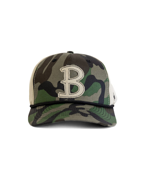 The Big B Twill Snapback - Woodland Camo is a 5 panel camo hat featuring green, brown, and black with a large white embroidered letter B on the front, displayed against a white background.