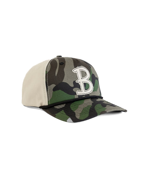 The Big B Twill Snapback - Woodland Camo is a 5-panel snapback cap with a camo front and brim, beige sides and back, and a large white embroidered 