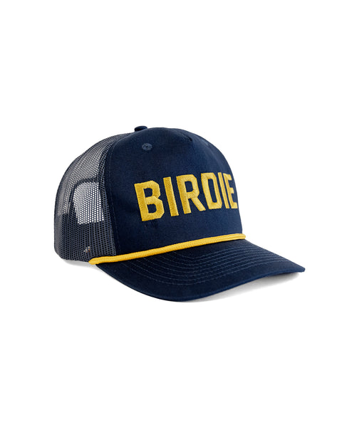 The Big Birdie Twill Trucker - Navy is a high crown snapback hat with yellow BIRDIE lettering, a yellow cord above the brim, black mesh sides and back, and a classic 5-panel cotton twill design.