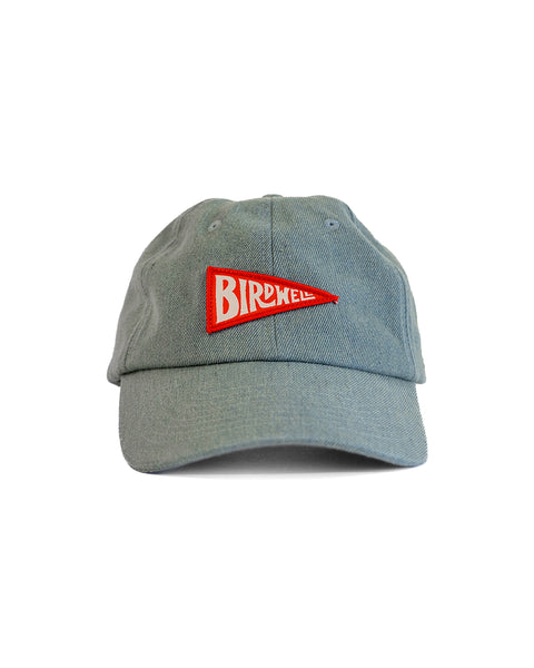 A medium wash Daddy Denim Hat features an unstructured dad style with a red triangular BIRDWELL patch on the front, shown against a white background.