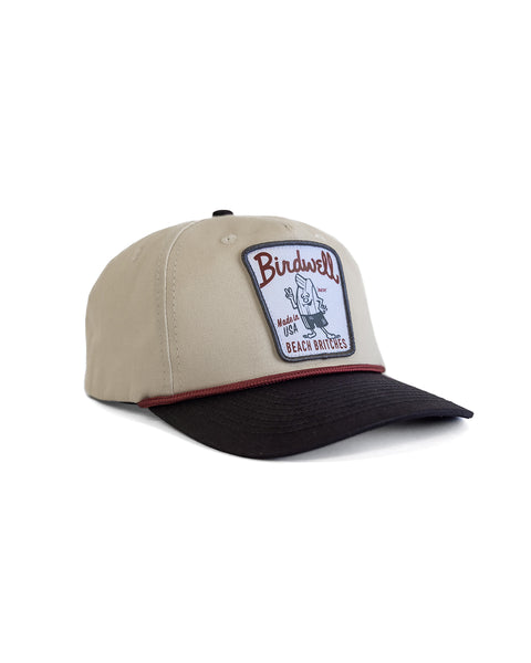 The Milkman Twill Snapback - Bone/Black is a beige 5-panel cotton hat with a black brim, maroon trim at the crown, and a front patch featuring 