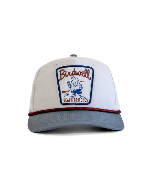The Milkman Twill Snapback - White/Federal Blue is a white 5-panel hat with a light gray brim, red piping, and a Birdwell Beach Britches patch featuring a cartoon bird—perfect for adding fun, classic style to your everyday look.