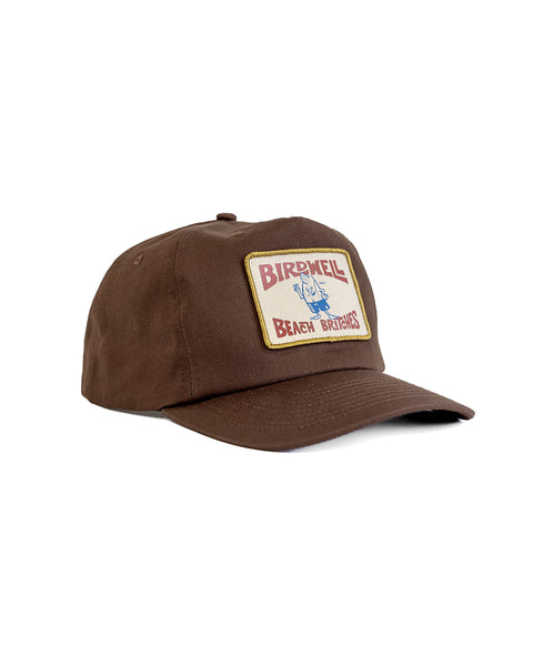 The OG Twill Snapback - Brown is a cotton hat featuring a yellow-bordered patch on the front that says Birdwell Beach Britches and displays a blue bird in red shorts.