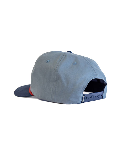 The OG Twill Snapback in Federal Blue/Navy is shown from the back, featuring a high crown, adjustable snapback closure, red accent on the left brim, and crafted from cotton twill, all set against a white background.