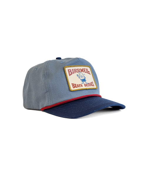 The OG Twill Snapback - Federal Blue/Navy is a blue cotton twill hat with a navy brim, red trim, and a rectangular patch reading BIRDWELL BEACH BRITCHES, featuring an illustrated blue bird character.