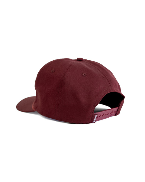 The Shield Twill Snapback - Burgundy is a maroon 5-panel cotton hat with a curved brim, stitched crown eyelets, and an adjustable snapback strap, shown from the back.
