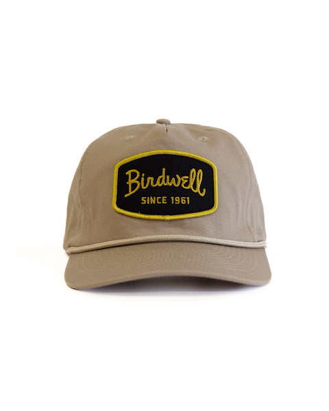 The Shield Twill Snapback - Tan is a cotton 5 panel hat featuring a black and yellow 