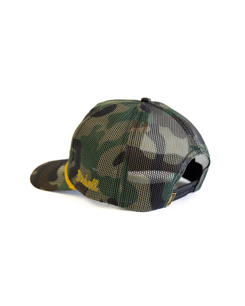 The Big Birdie Twill Trucker - Woodland Camo is a cotton snapback hat with a black mesh back and adjustable strap, shown from the rear on a white background. Partially visible yellow text appears on the left side.
