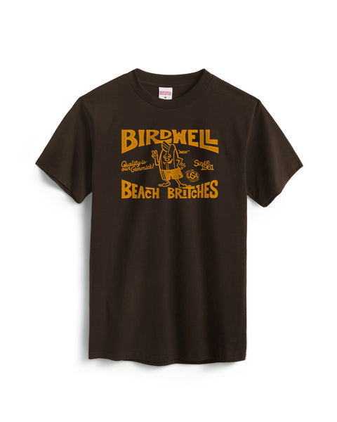 The Taggert T-Shirt - Java is a dark brown, garment-dyed heavyweight cotton tee featuring yellow Birdwell Beach Britches text, a central cartoon figure in shorts, decorative graphics, and pre-shrunk for comfort.
