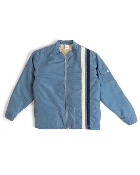 The Quilt Lined Racing Jacket in Federal Blue features a beige and navy vertical stripe on the right side, long sleeves, and a small pocket on the left sleeve.