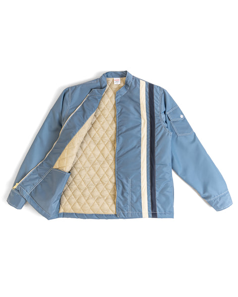 The Quilt Lined Racing Jacket in Federal Blue/Bone/Navy features cream and navy vertical stripes on one side, a zippered front, a sleeve flap pocket, and a quilted cream lining. The jacket is shown laid flat with one side open to display the lining.