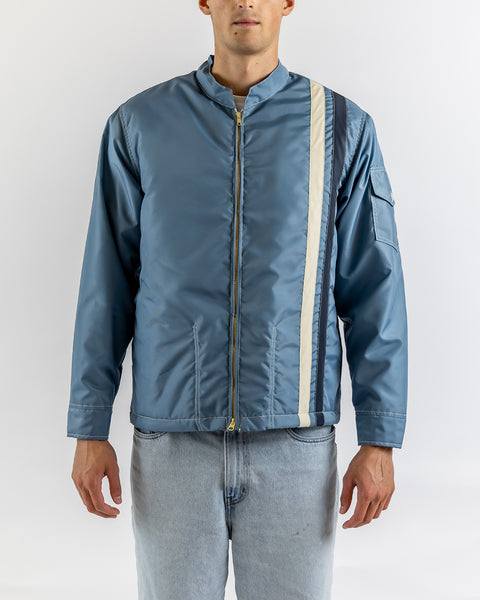 A person wears the Quilt Lined Racing Jacket in Federal Blue/Bone/Navy with vertical stripes, paired with light blue jeans, standing against a plain white background.