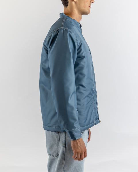 A man stands in profile wearing the Quilt Lined Racing Jacket in Federal Blue/Bone/Navy and light blue jeans against a plain white background.