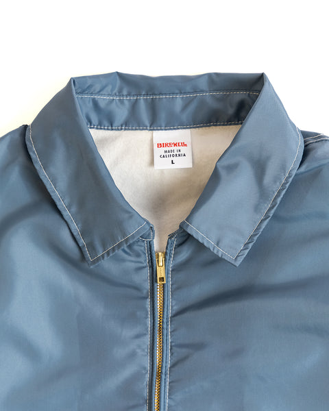 A close-up of the Comp Jacket 25 in Federal Blue/Bone, featuring a collar and partially unzipped to reveal a BIRDWELL MADE IN CALIFORNIA L tag, highlights its American-made SurfNyl durability.