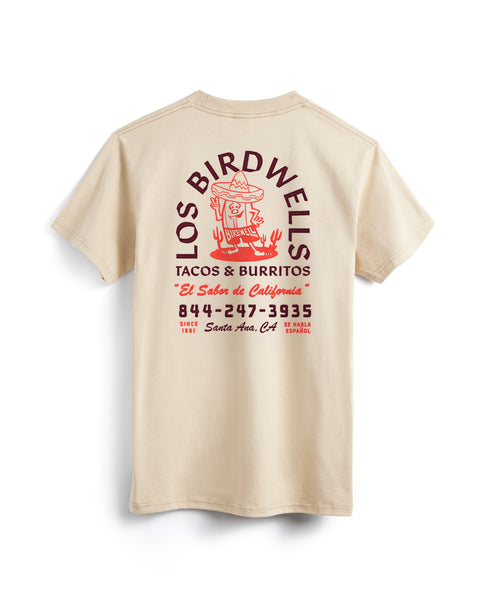 The Los Birdwells T-Shirt - Cream is a heavyweight 100% cotton tee with a red back graphic featuring a cartoon taco in a hat, LOS BIRDWELLS TACOS & BURRITOS text, Spanish phrases, and a phone number styled like a Mexican restaurant ad.