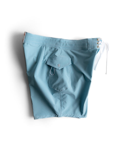 The 808 SurfStretch Side Pocket Boardshorts in light blue feature a side lace-up waistband, white drawstrings, and a back pocket with button flap—classic boardshort style shown on a white background.